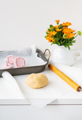 Preparation of the dough for making cookies with molds in the form of flowers, a rolling pin, a bouquet of orange flowers and a baking tray. Concept of family and cooking.