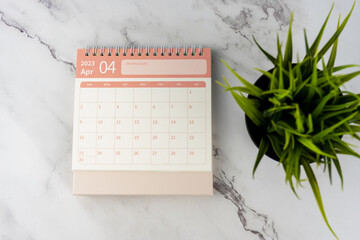 April 2023 desk calendar on marble table flat lay with potted plant