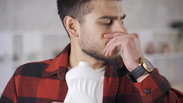 Young man smelling a spoiled product is disgusted by the smell.
Young man sniffing a spoiled product in his hand is covering his nose because it smells bad.
