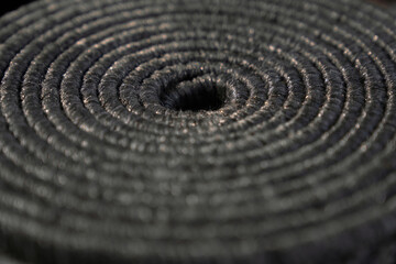 Fototapeta na wymiar Twisted, coiled natural dark jute pattern as background. Close up of textured backdrop of tight rolled up grey rope, with void in middle, with blurring. Concept of textures and backgrounds. 