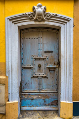 An old blue door with peeling paint and a yellow wall