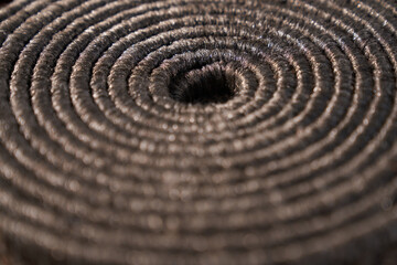 Fototapeta na wymiar Textured backdrop of rolled up grey carpet edge, with small void in middle. Close up of brown rope folded in tight spiral background, pattern with copy space. Concept of textures and backgrounds. 