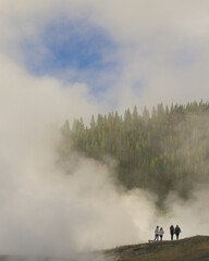 Four tourists below steamy tree line at dawn at Yellowstone National Park, Wyoming