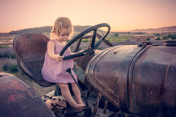 Cute girl on an old tractor. A small child farmer operates agricultural machinery