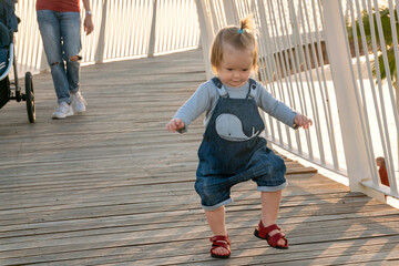 Summer day in nature. Toddler walks on a wooden bridge. Walk in the park for a small child