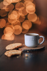 cup of coffee and cookies on dark table with glittering lights background