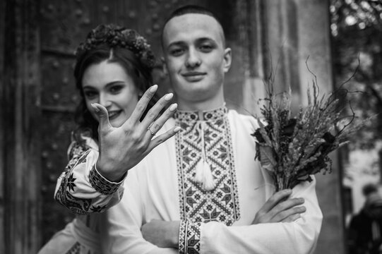 black and white photo, Emotional portrait of happy young couple in love, family hugging, holding hands, running in Lviv city in traditional Ukrainian shirts. Young people hug in the old town of Lviv