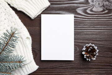 Christmas greeting card mockup with green fir tree branches and knitted sweater on brown wooden background, top view, flat lay. Blank New Year holiday card mock up with decoration