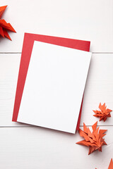 Christmas card mockup with envelope and red paper fir trees on white wooden background, top view, flat lay