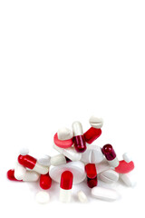 Red and white capsules and tablets and medicines stacked close-up on a cropped white background.