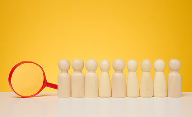 Wooden figures of men stand on a yellow background and a red plastic magnifying glass. Recruitment concept