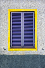 A window with purple shutters and a yellow painted frame