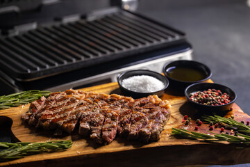 ribeye steak on wooden board with spices and electric grill