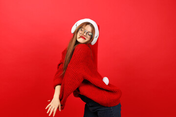 A young woman in festive clothes dancing to the music on a red background. Positive and cheerful celebration of the new year and Christmas.