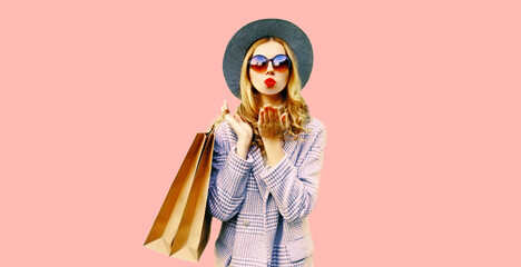 Autumn portrait of beautiful young woman with shopping bags blowing her lips sends air kiss with lipstick wearing coat, round hat on pink background