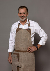 A mature man in a chef's apron with an oven mitt is standing and smiling.