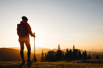 Hiker with backpack standing on top of a mountain and enjoying sunset. Woman successful hiking...