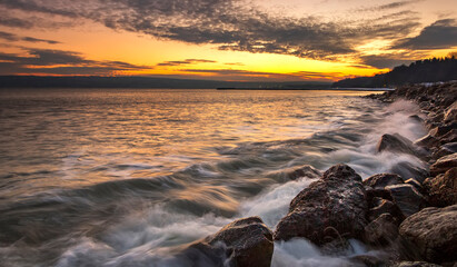 Sunset over the sea with splash waves on the rocks