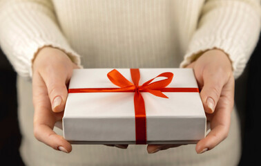 White gift box with red ribbon in beautiful female hands. Holiday concept