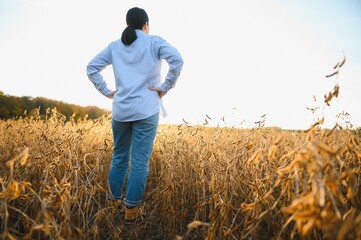 Portrait of young female farmer standing in soybean field examining crop.