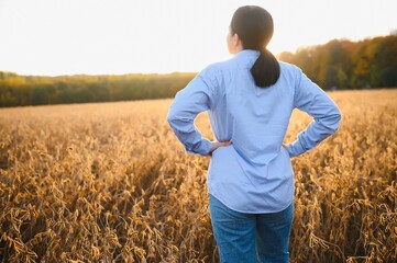 A young female farmer is working in a soybean field at sunset.