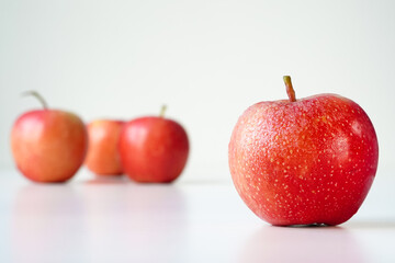 One red gala apple close-up on white, space for text. Orange red rounded ripe fruit with yellowish speckles, at eye level, several apples in the distance in a blur, light background