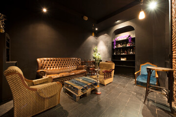 A relaxing space in a bar with armchairs upholstered in leather and vintage fabric and black walls
