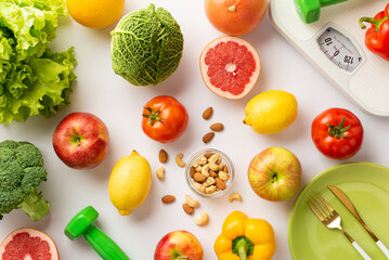 Proper diet concept. Top view photo of vegetables fruits nuts plate cutlery dumbbells and scales on isolated white background