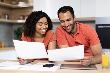 Cheerful millennial black lady and guy in red t-shirts work with documents, check bills, calculate profit in kitchen