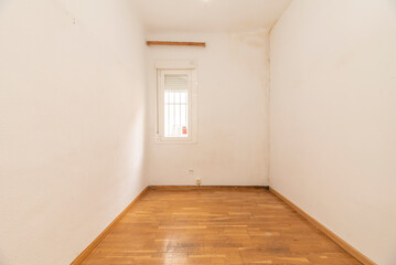 Empty living room with white painted walls, small white aluminum plate window with bars and loose floating oak flooring