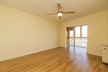 Empty living room with cream painted walls, glazed bay window with tongue and groove wood and four-blade ceiling fan