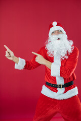 Fototapeta na wymiar Portrait von einem verkleideten Weihnachtsmann, der auf einen Platzhalter zeigt und isoliert vor roten Hintergrund ist