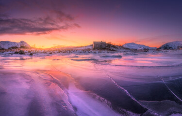 Frozen sea coast and house at colorful sunrise. Winter in Lofoten islands, Norway. Snowy mountains,...