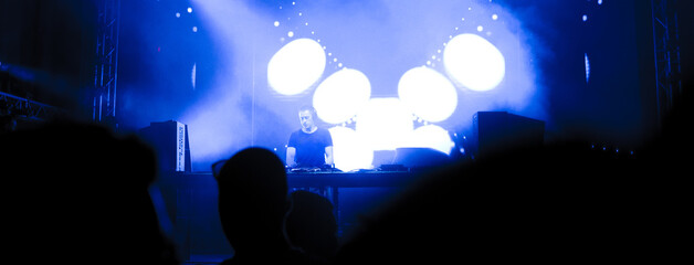 Dj playing techno music on the concert stage at summer night