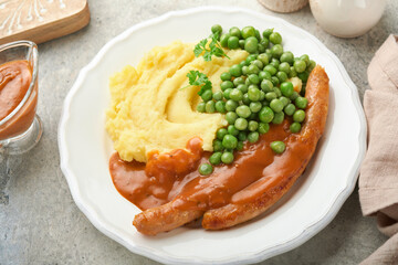 Bangers and mash. Grilled sausages with mash potato and green pea on white plate on grey background. Traditional dish of Great Britain and Ireland. BBQ beef sausages. Top view.