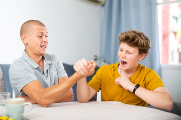 Fototapeta premium Young boy competing with his father in arm wrestling on kitchen table.