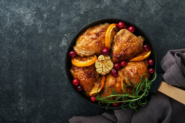 Baked chicken thighs with orange, cranberry and spicy herbs rosemary servered in frying pan on black concrete background. Festive Christmas Dinner Concept menu. Top view. copy space