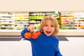 Fototapeta na wymiar Child with fresh tomato vegetables. Kid choosing food in grocery store or a supermarket. Fruit and vegetable.