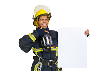 Fototapeta premium Young smiling African American fireman wearing uniform and helmet looking to the camera and holding blank paper sheet in hand and finger pointing. Copy space for text, isolated on white background 
