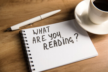 The inscription on the notepad what are you reading and a cup of coffee