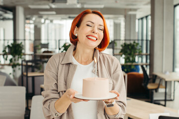 Happy businesswoman holding Birthday cake while making surprise party with her colleagues in the office.