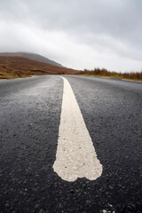 White line on a road leading to mountain in the background. Cloudy sky. Travel and transportation...