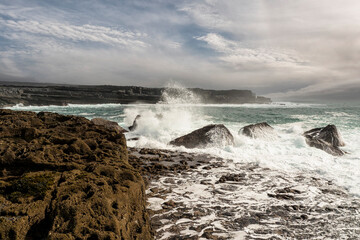 Powerful ocean wave hits rough stone coast of Aran Island, county Galway, Ireland. Rough nature scene. Water splash. Power of nature. Cloudy sky. Irish landscape. Popular tourist area