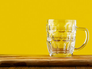 Empty massive beer glass jar on a wooden table. Yellow background.