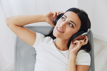 Woman listening to music on headphones at home on a chair, happiness and relaxation on her day off