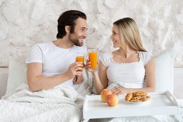 Loving caucasian couple having breakfast in bed together, spending honeymoon morning at modern hotel