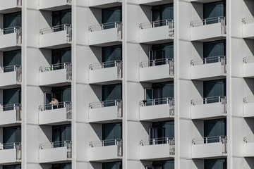 A woman standing alone on a balcony of an big hotel facade 