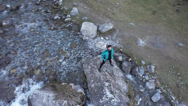 LGBTQ person playing with drone camera and hands, standing on a rock surrounded by water