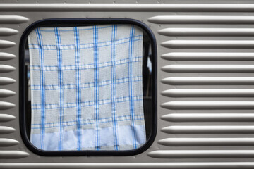 Motor Home Vehicle Detail Background / Silver streamlined travel trailer window covered by dish towel (copy space) - 553325925