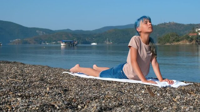 Bhujangasana pose at sea morning. A pretty teen training on the shore and stretching during bhujangasana pose on the pebbles shore in the summer morning.